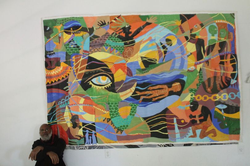 a picture showing moyo okediji sitting next to his artwork