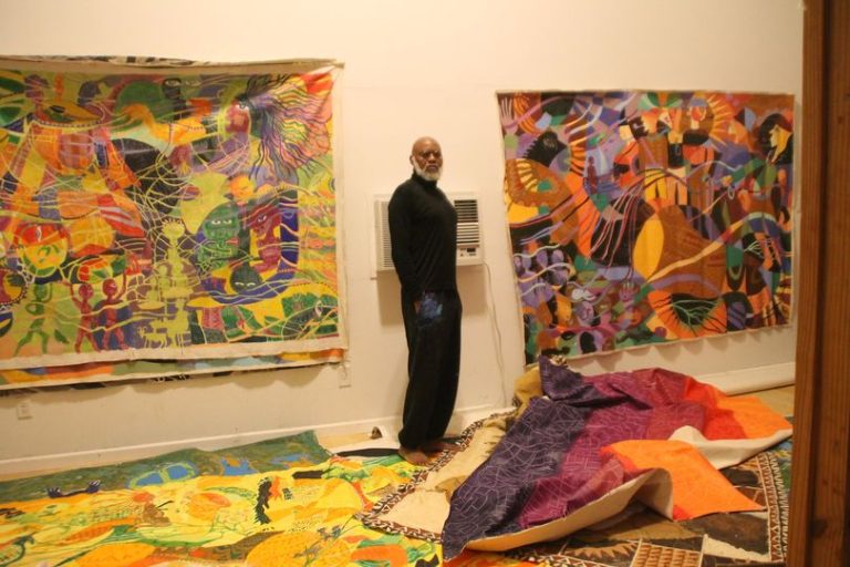 a picture of moyo okedij in his art gallery and around him is his art pieces