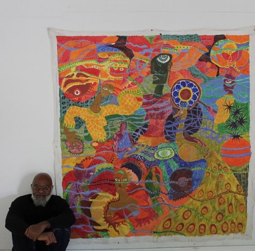 a picture showing moyo okediji sitting next to his artwork