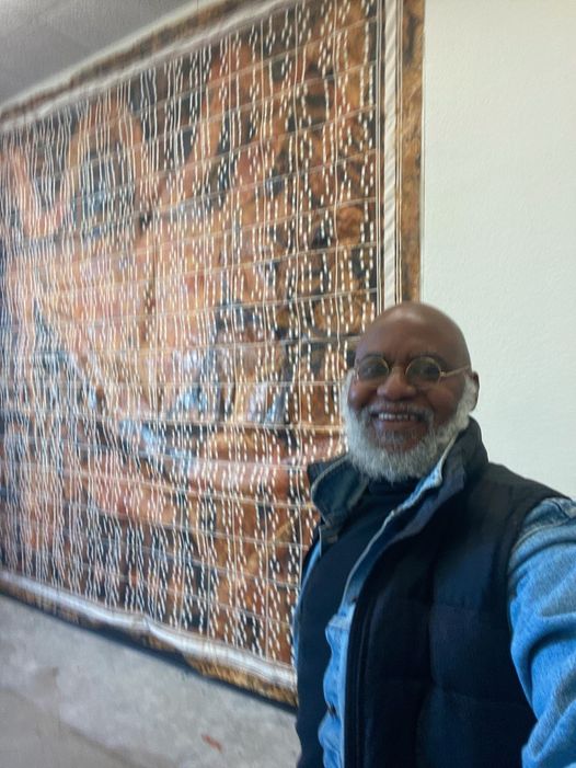 a picture showing moyo okediji standing next to his artwork