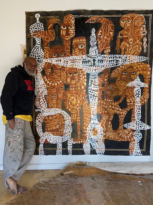 a picture showing moyo okediji sitting next to his artwork which started in 2019 and ended in 2020