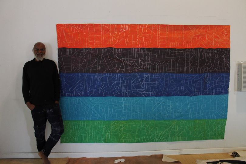 a picture showing moyo okediji standing next to his artwork