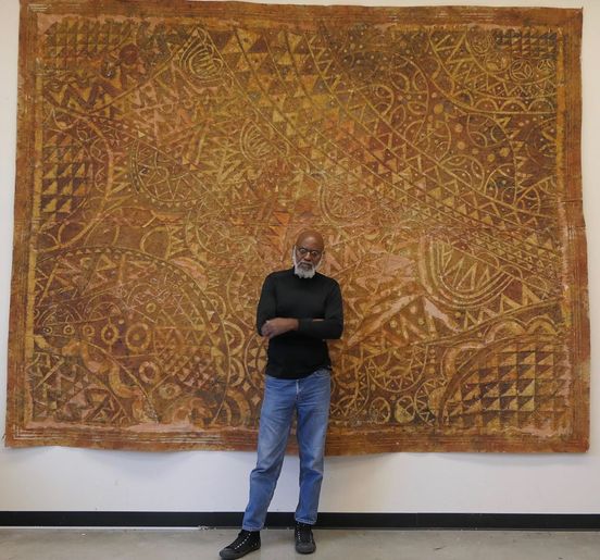 a picture showing moyo okediji standing next to his artwork