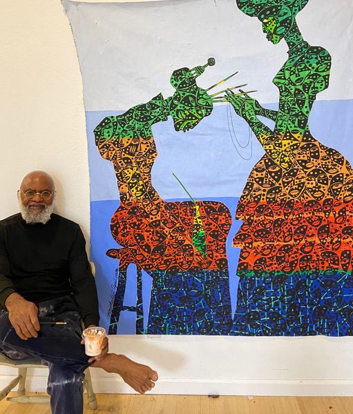 a picture showing moyo okediji sitting next to his artwork