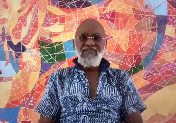 a picture showing moyo okediji sitting next to his artwork