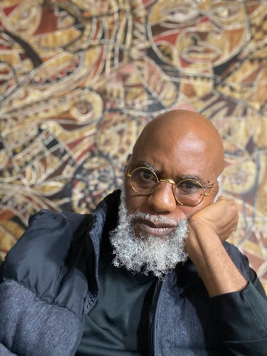 a picture showing moyo okediji in front of one of his art piece poised for the camera