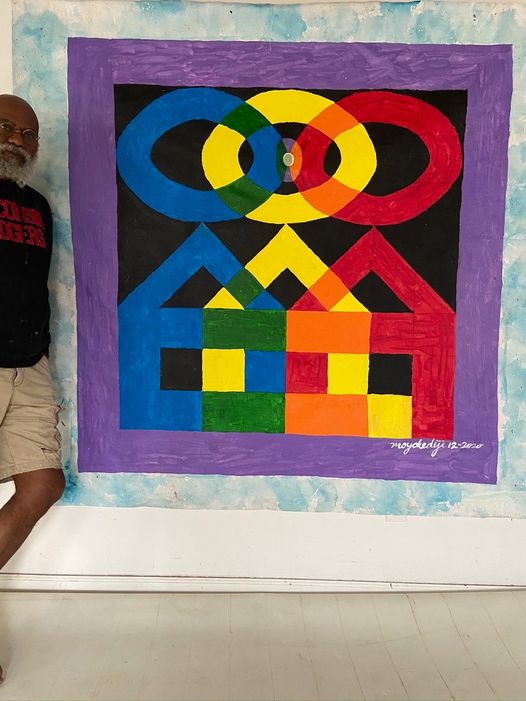 a picture showing moyo okediji standing next to his artwork