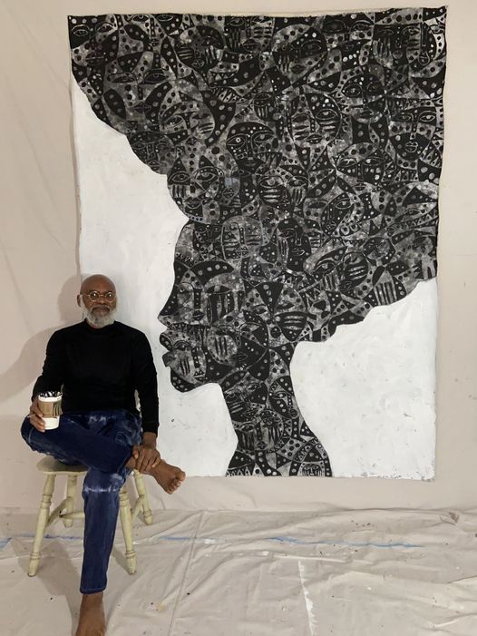 a picture showing moyo okediji sitting next to his artwork