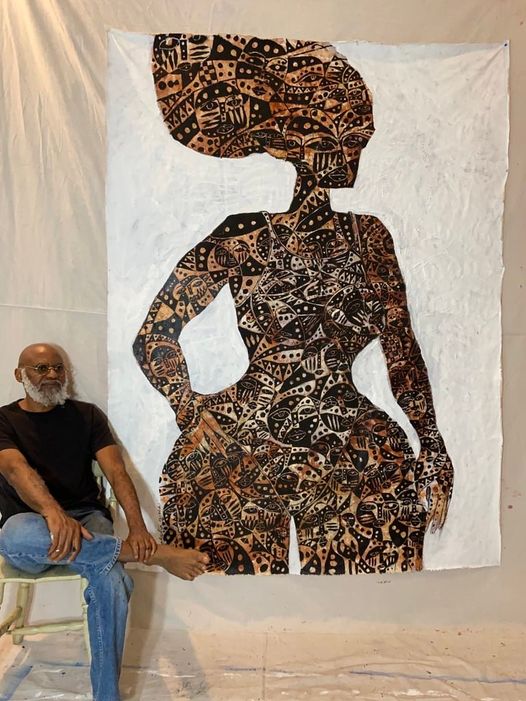 a picture showing moyo okediji sitting next to his artwork