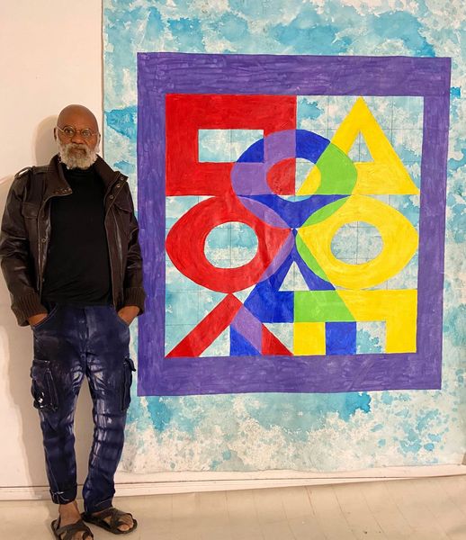 a picture showing moyo okediji standing next to his artwork