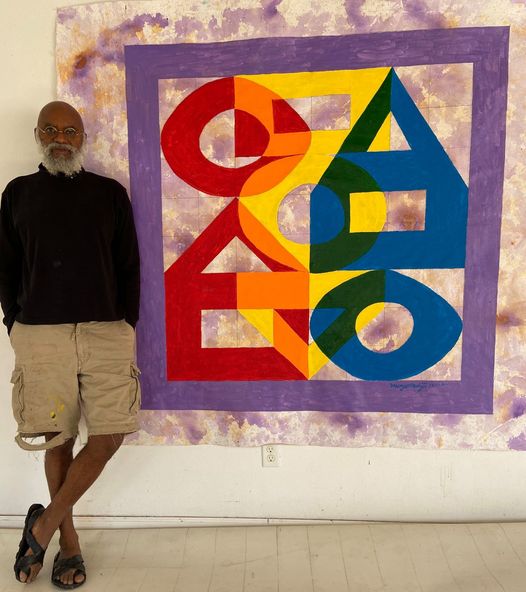 a picture showing moyo okediji standing next to his artwork