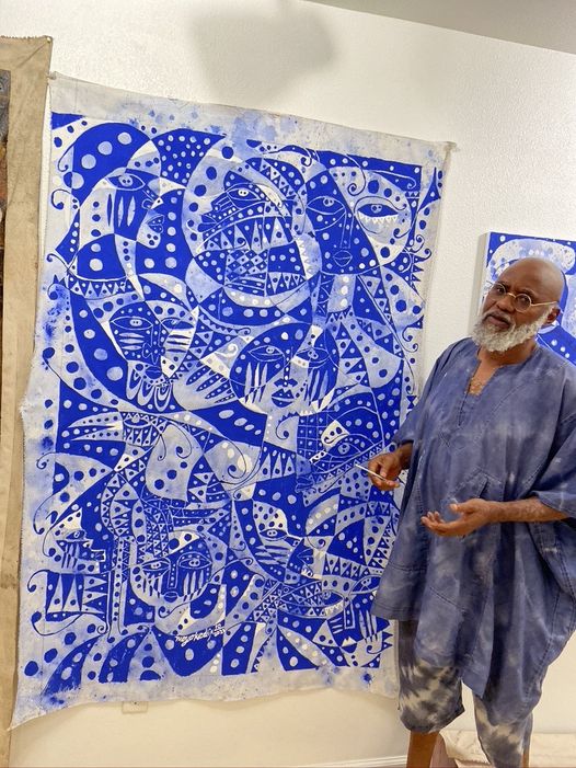 a picture showing moyo okediji standing next to his artwork