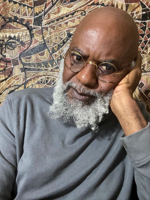 a picture showing moyo okediji sitting in fornt of his artwork with his hand placed in his chin