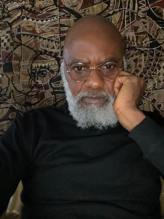 a picture showing moyo okediji sitting next to his artwork