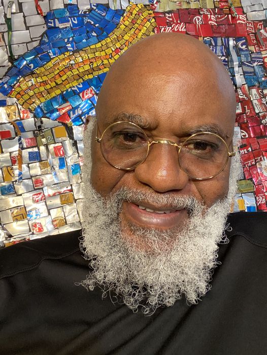 a picture showing moyo okediji sitting next to his artwork