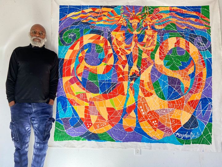 a picture showing moyo okediji standing next to his artwork