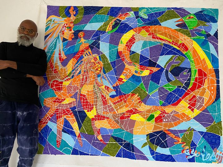 a picture showing moyo okediji sitting next to his artwork