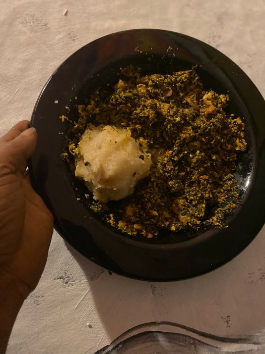 A picture showing moyo okedijis hand holding a bowl of vegetable soup and garri