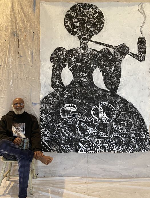 a picture showing moyo okediji sitting next to his artwork