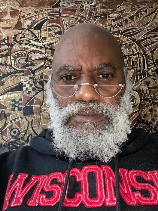 a picture showing moyo okediji sitting next to his artwork