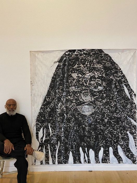 a picture showing moyo okediji sitting next to his artwork