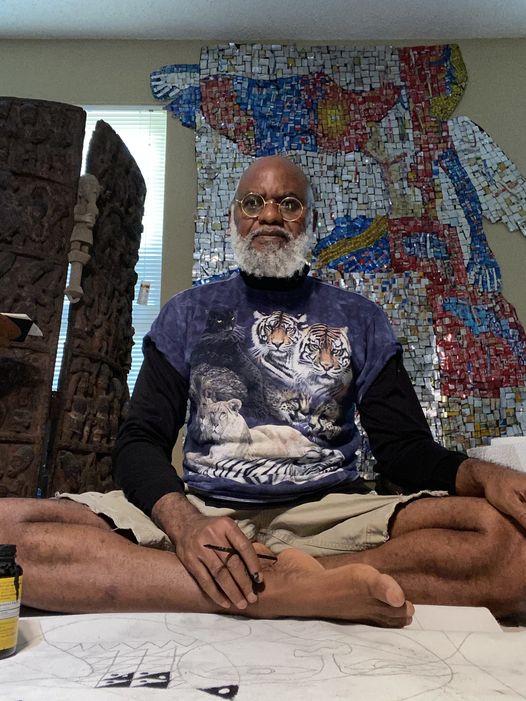 a picture showing moyo okediji sitted on the floor with his artwork behind him