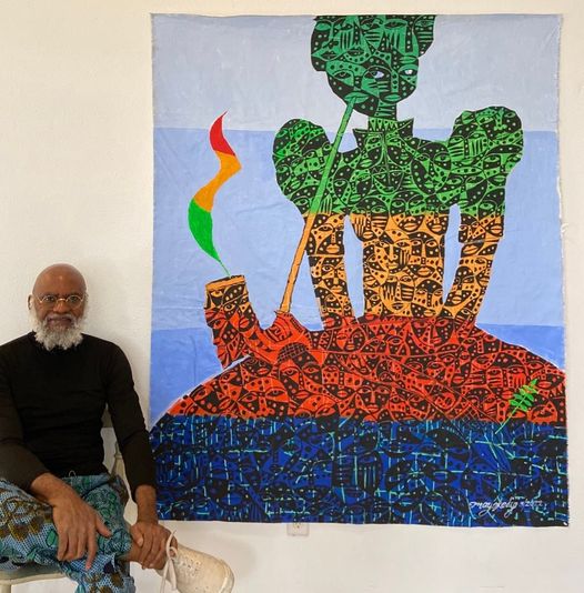 a picture showing moyo okediji sitting next to his artwork