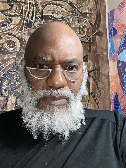 a picture showing moyo okediji sitting behind his artwork