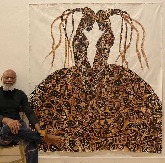 a picture showing moyo okediji sitting next to his artwork