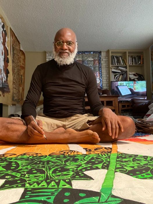 a picture showing moyo okediji sitted on the floor in is gallery with his artwork behind him