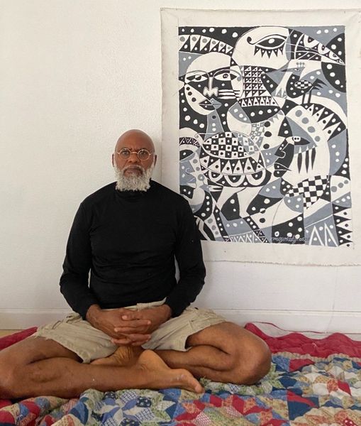 a picture showing moyo okediji sitting next to his artwork