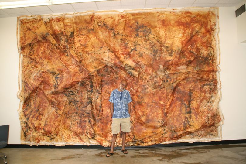 a picture showing moyo okediji standing next to his artwork