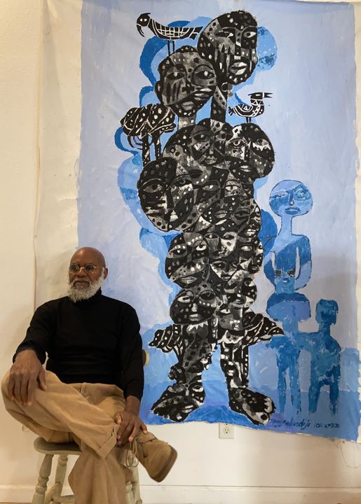 a picture showing moyo okediji sitting next to his artwork