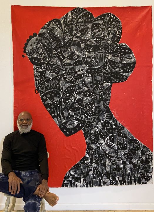 a picture showing moyo okediji sitting next to his artwork