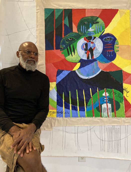 a picture showing moyo okediji sitting next to his artwork